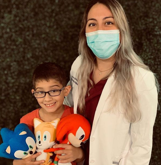 A child holding stuffed toys and standing next to a pediatric dentist.